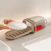 A hand holds a portable travel soap box with a drainage lid, showing the textured silver and beige container.