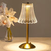 A gold-toned table lamp with a clear pleated shade illuminates a white orchid flower.