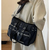 A black nylon shoulder bag with chain accents is carried by a person wearing a beige coat.