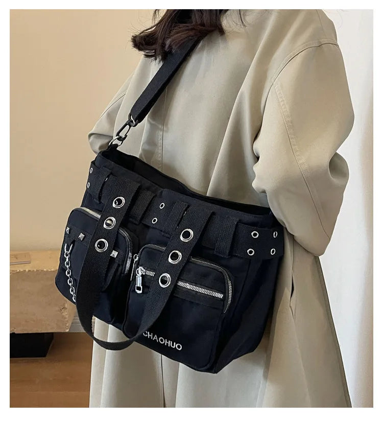 A black nylon shoulder bag with chain accents is carried by a person wearing a beige coat.
