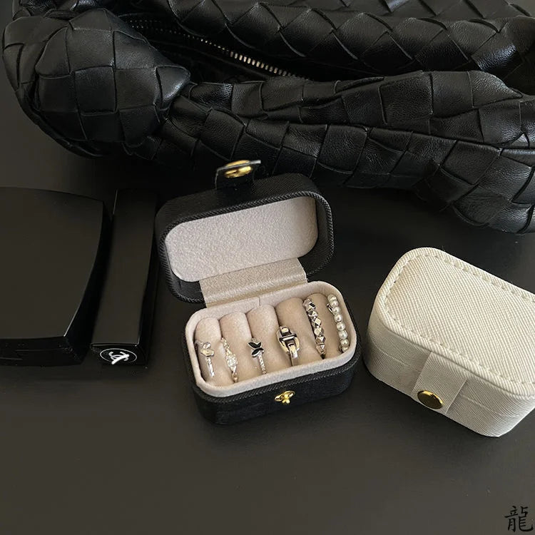 A black quilted leather jewelry travel case is shown open, displaying several silver and gold rings and earrings.