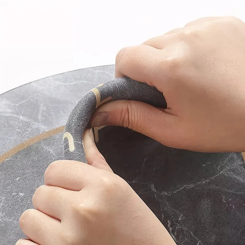 A hand is holding a dark gray diatomite bath mat with a gold accent on a black stone surface.