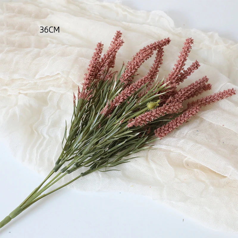 Ein Zweig künstlicher Lavendel mit rosa-violetten Blüten auf einem durchsichtigen beige Stoff.