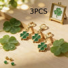 Three green four-leaf clover keychain charms displayed on a wooden surface with a framed clover.