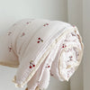 A rolled pink floral muslin baby blanket with red cherries is shown against a light background.