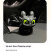 A black Toothless car ornament featuring glowing green eyes and up and down flapping wings.
