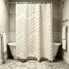 A cream-colored bohemian floral cutout tassel shower curtain hanging on a rod in a bathroom.