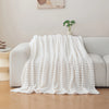 A white brushed flannel throw blanket draped over a light gray sofa in a bright living room setting.