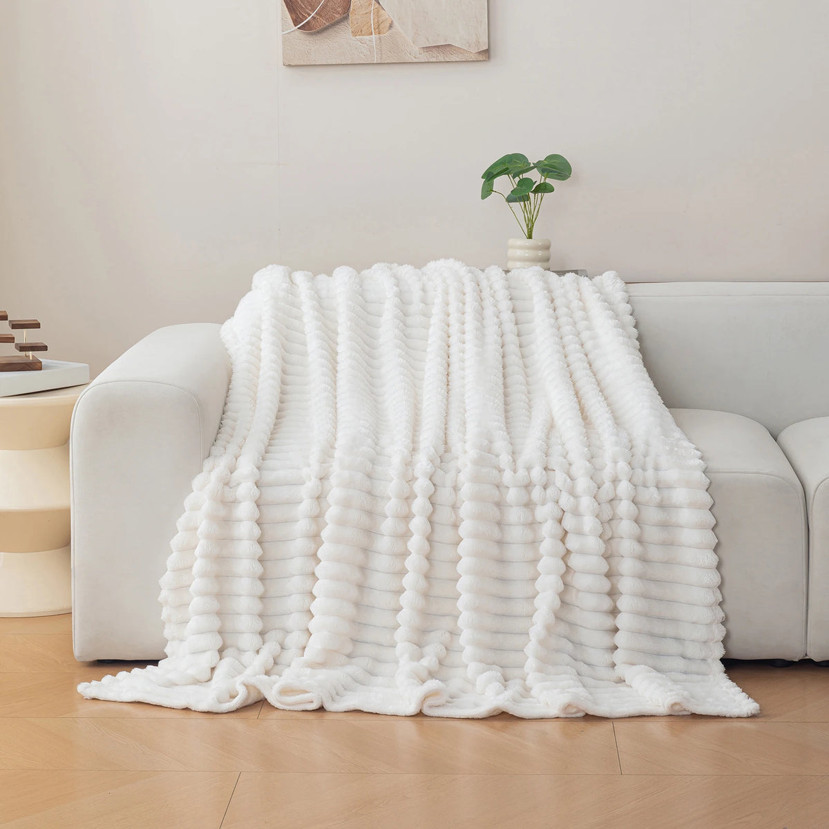 A white brushed flannel throw blanket draped over a light gray sofa in a bright living room setting.