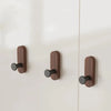 Three wooden walnut wood hooks mounted on a white wall for entryway or bathroom organization.