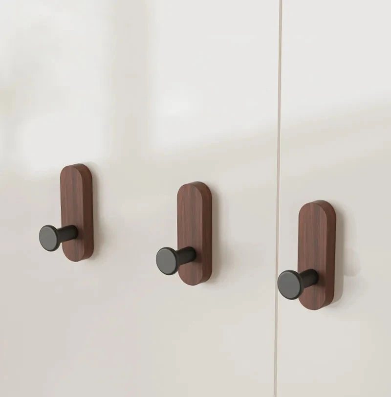 Three wooden walnut wood hooks mounted on a white wall for entryway or bathroom organization.