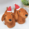 A pair of brown plush dog slippers with red and white Santa hats, resembling a dachshund's head.