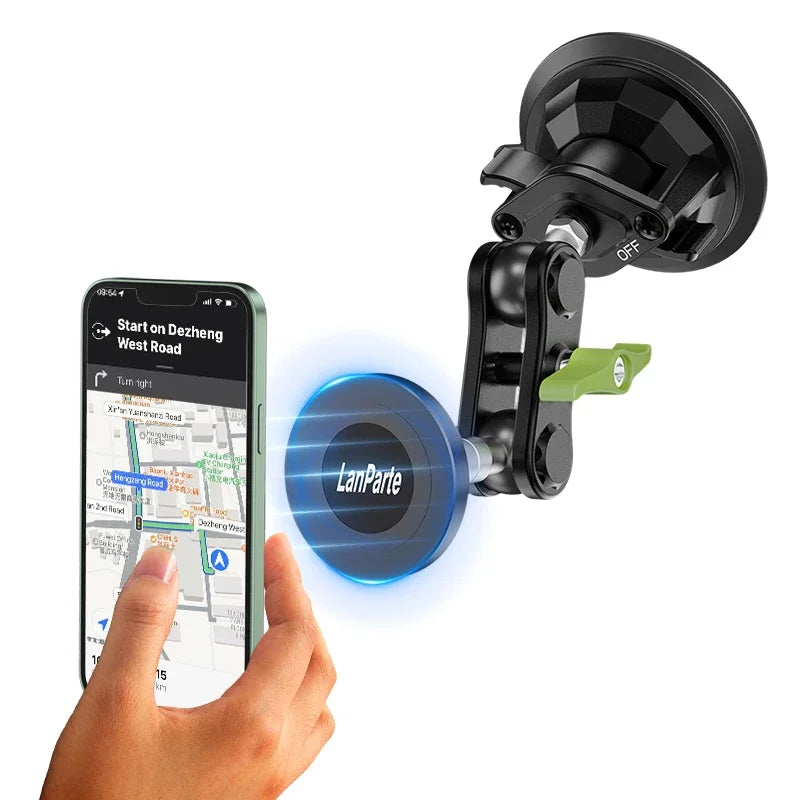 A hand holds a smartphone displaying a map, next to a black magnetic car phone mount with a green attachment.