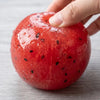 Une main serre un jouet anti-stress en watermelon rouge vif, montrant sa texture moelleuse.