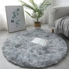 A round, fluffy gray shaggy area rug placed on a light wooden floor next to a potted plant and framed artwork.