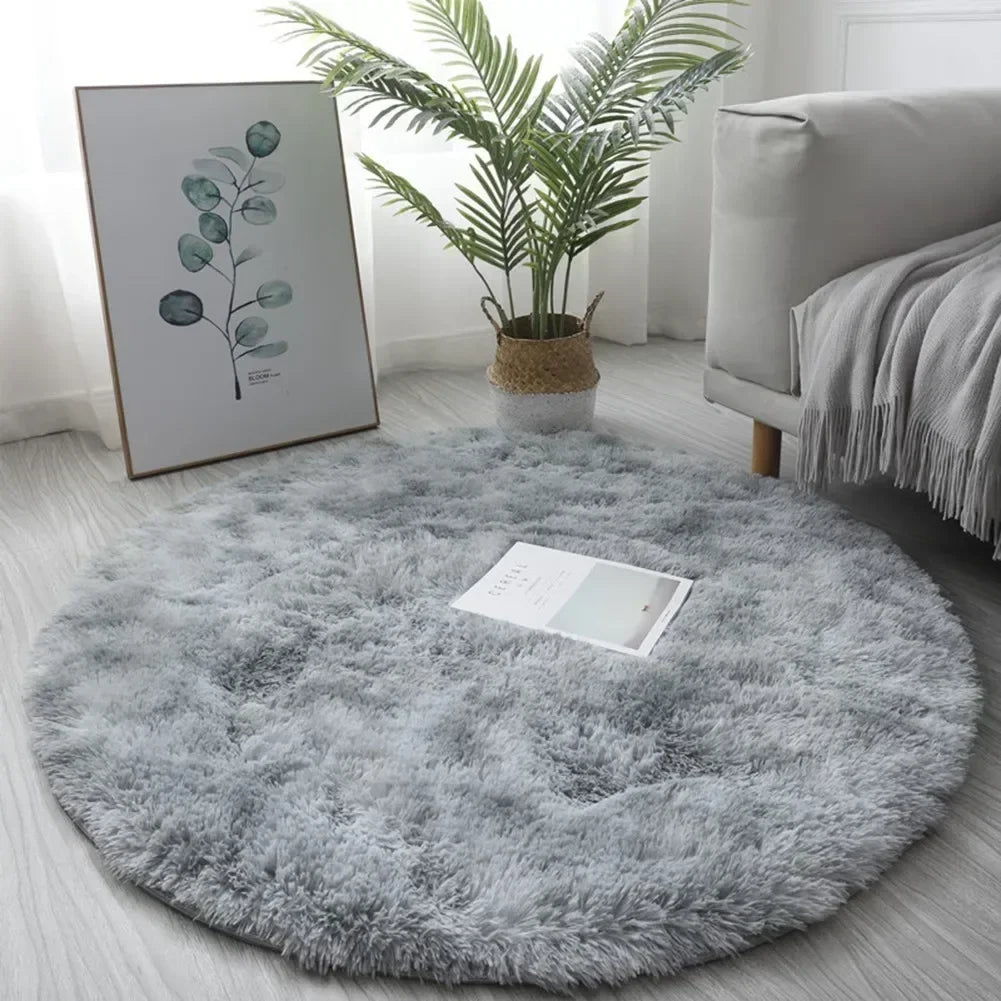 A round, fluffy gray shaggy area rug placed on a light wooden floor next to a potted plant and framed artwork.