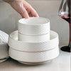 A stack of white ceramic soup bowls is shown with a hand placing a bowl on top.
