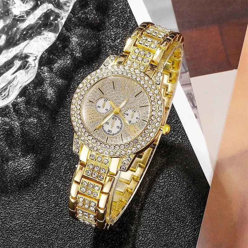 A gold rhinestone watch with a textured face and bracelet is displayed on a dark surface.