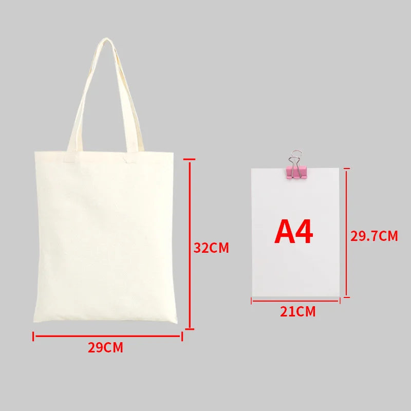 A white canvas shopping tote bag with handles shown next to an A4 sized piece of paper for scale.
