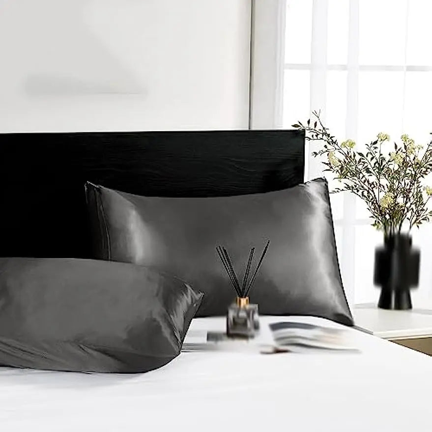 Un juego de almohadas de seda satén gris oscuro sobre una cama blanca con una ventana y arreglo floral.