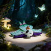 A plush toy of a Luna moth with teal and purple wings resting on a light-colored surface in a dark, forest-like setting.