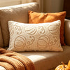 A beige sofa with an orange pillow and a cream plush throw pillow on it, next to a golden pumpkin.