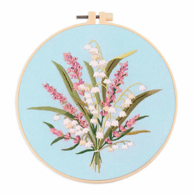 A circular embroidery hoop featuring a floral design of pink and white wildflowers on a light blue background.