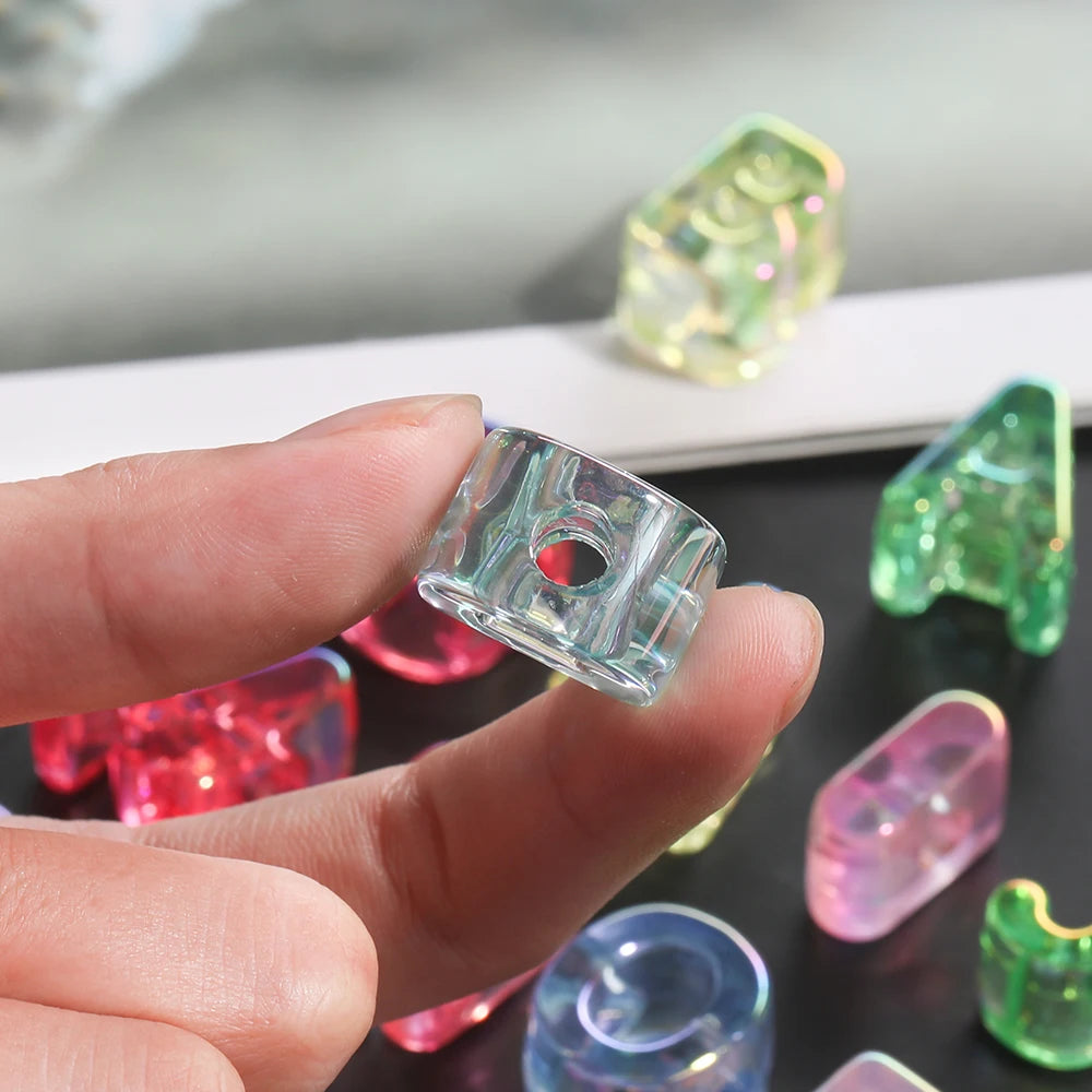 A hand holds several clear and colored acrylic alphabet beads for jewelry making.
