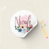 A white sticker with the name Nicole written in elegant script surrounded by pink and blue floral elements.