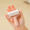 A hand is holding a pink mini portable lint roller with a white roller, demonstrating the product.