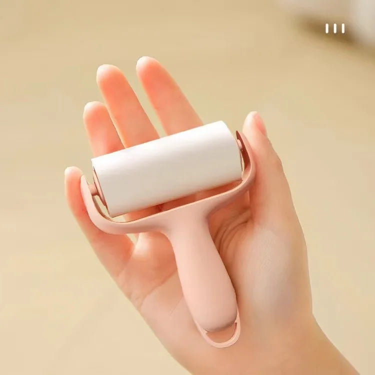 A hand is holding a pink mini portable lint roller with a white roller, demonstrating the product.