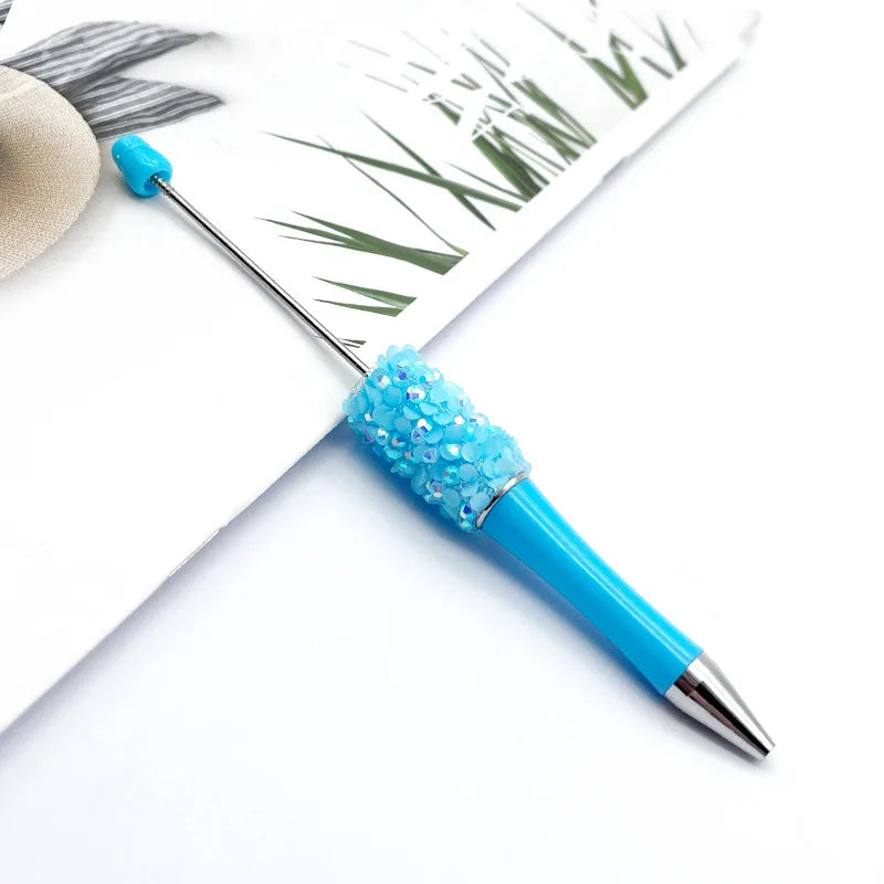 A close-up of a sparkling blue ballpoint pen with a sequin tip resting on white paper.
