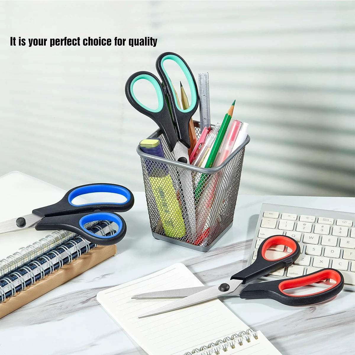 A collection of stainless steel scissors and pens in a gray organizer basket on a white desk.
