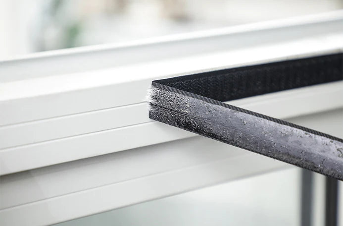 Close-up of a black reusable self-adhesive mosquito window screen being applied to a white window frame.