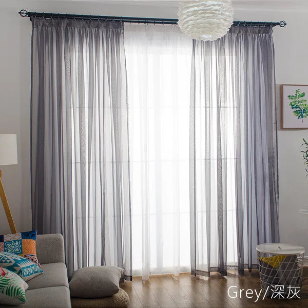 Grey sheer voile curtains with rod pockets filtering light through a window.