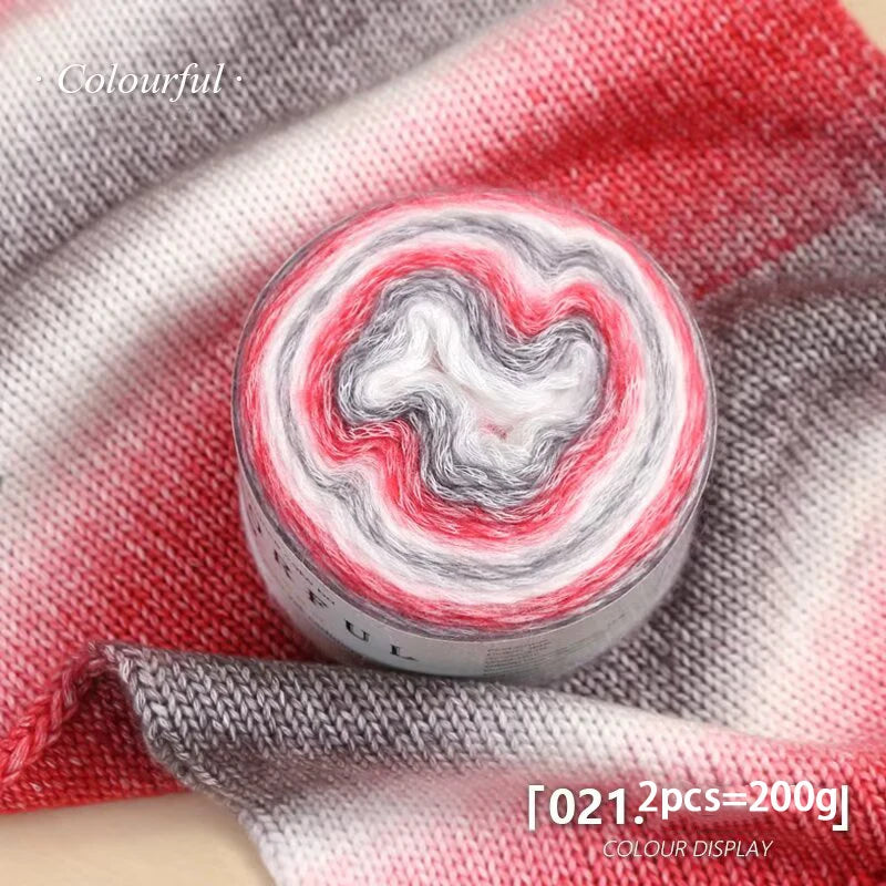 Roll of colorful gradient cake yarn showing red and white swirls on a gray fabric background