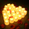 A close-up of twelve glowing LED tea lights arranged on a dark surface, surrounded by red rose petals.