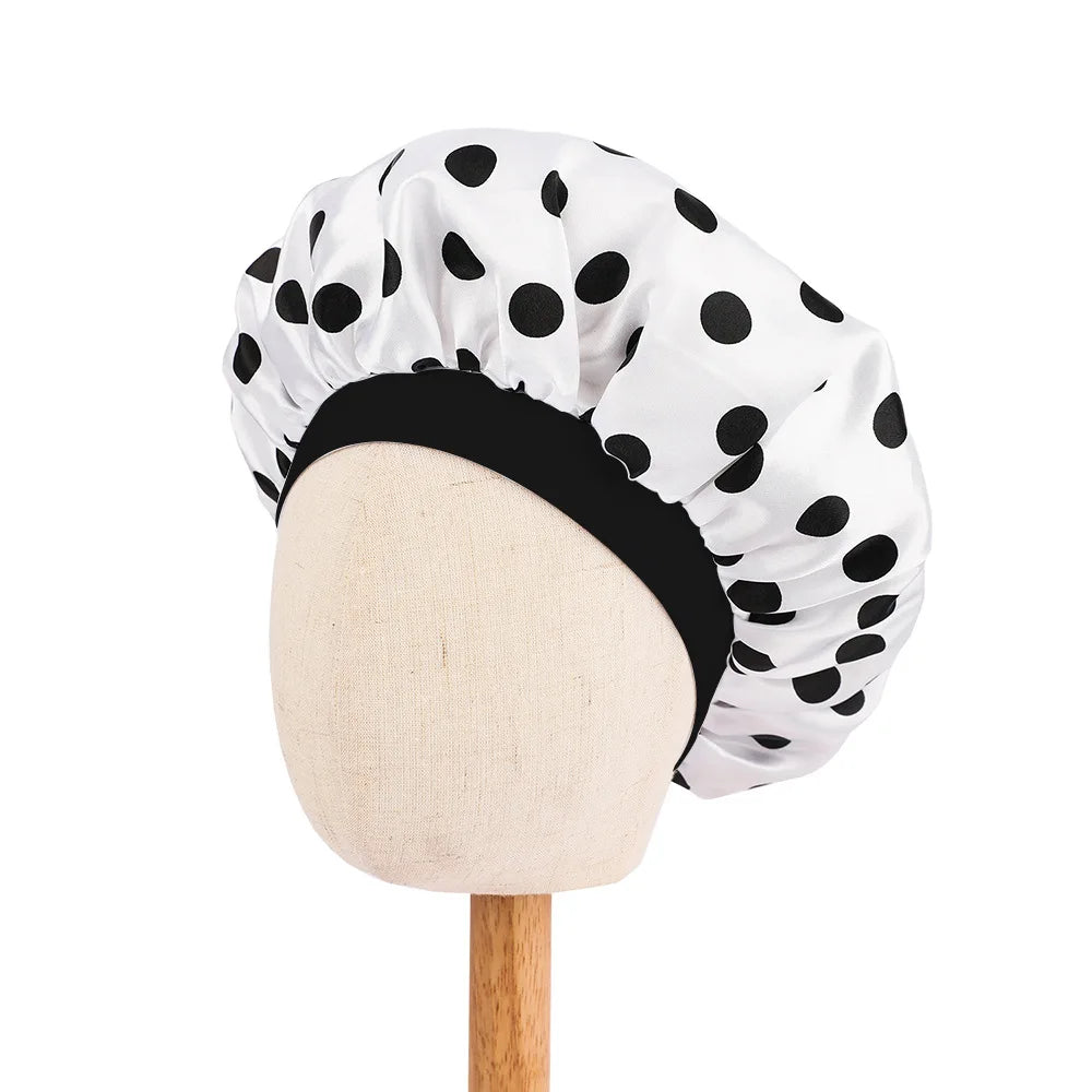 White satin sleep cap with black polka dots and a black band displayed on a wooden mannequin.