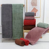 A stack of various colored bath towels, including gray, green, and pink, displayed on a wooden rack.