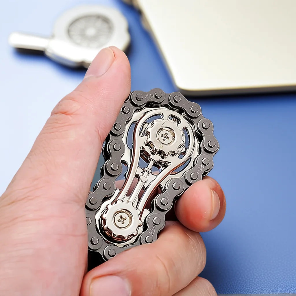 A hand holds a silver sprocket fidget spinner with iridescent details on a blue surface.