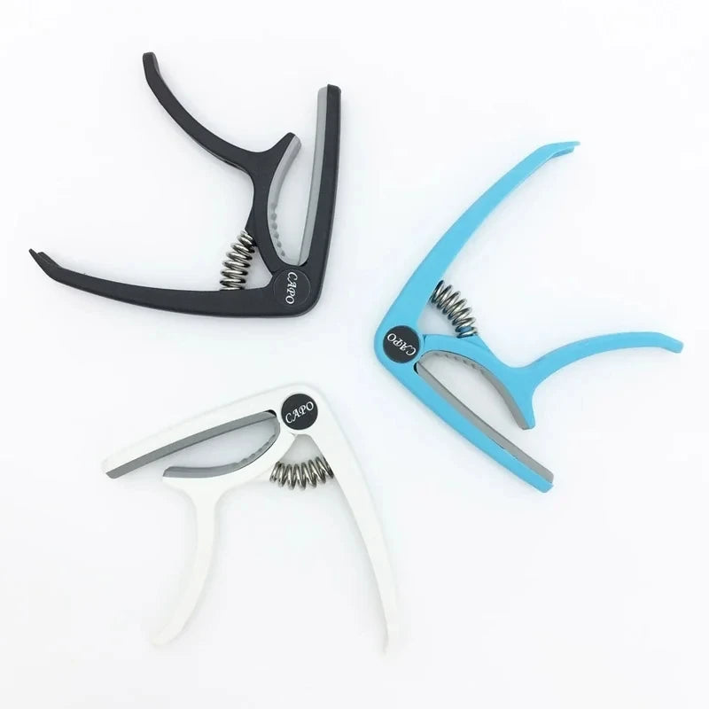 Three adjustable guitar capos in black, blue, and white with built-in bridge pin pullers.