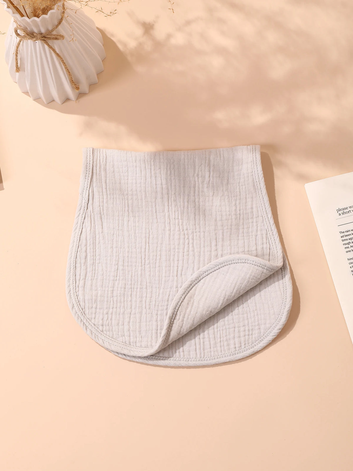 A light beige, quilted baby burp cloth is shown flat on a pink background.