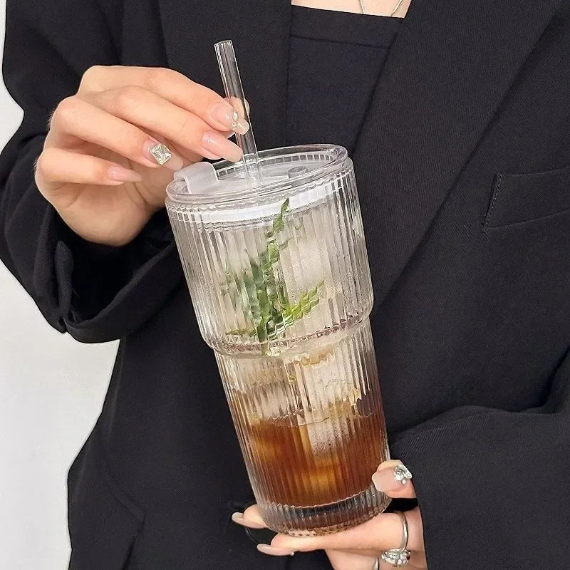 Une main tient un verre à tranches rayées avec un couvercle et une paille contenant du thé glacé ou une boisson.