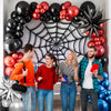 A group of four people posing in front of a balloon garland arch featuring red, black, and silver balloons.