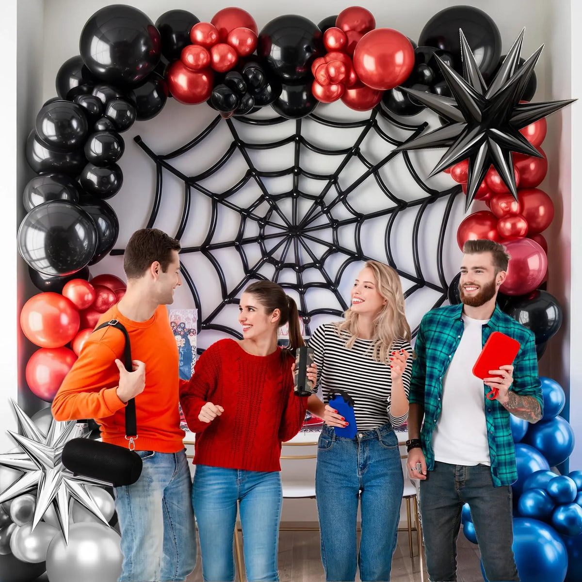 A group of four people posing in front of a balloon garland arch featuring red, black, and silver balloons.