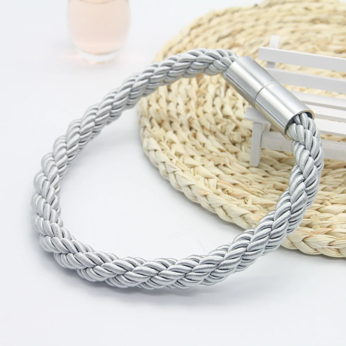 Silver rope magnetic curtain tiebacks with a metal clasp resting on a woven mat
