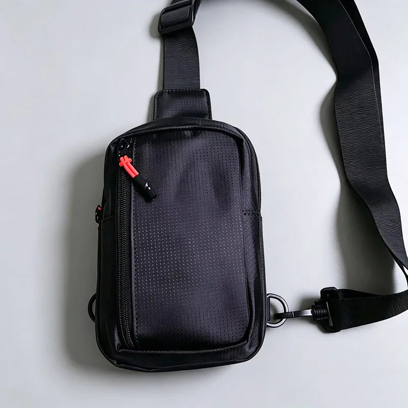 A black compact water-resistant sling bag with a strap is shown against a light gray background.