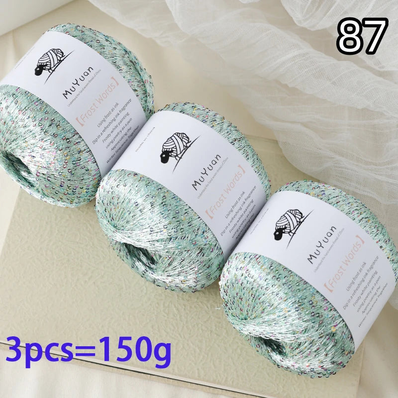 Three balls of glitter yarn labeled MuYuan Frost Words are displayed on a light surface.