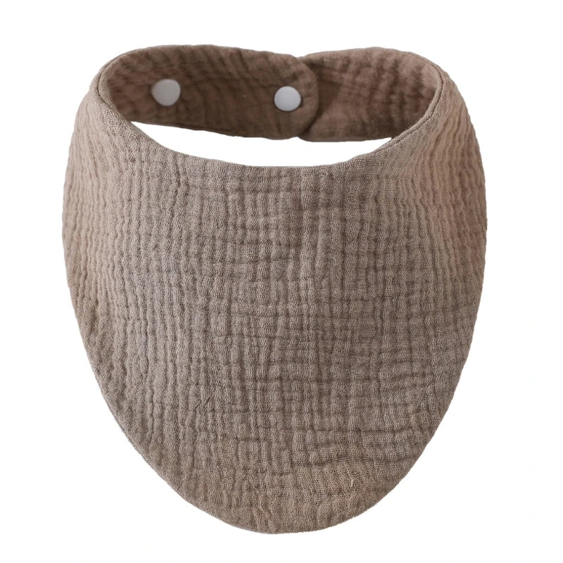 A round, beige organic cotton muslin baby bib with a gathered top and absorbent band.