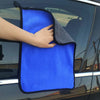 A hand is holding a bright blue microfiber car drying towel against the window of a vehicle.